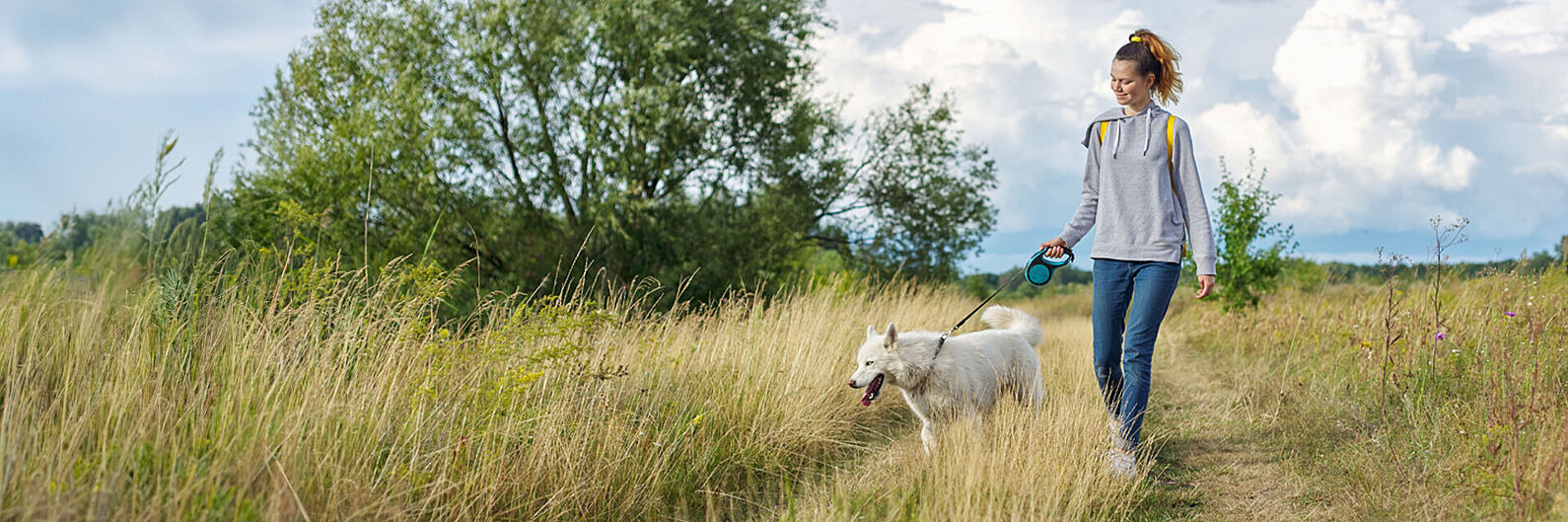 Eine Frau läuft mit ihrem Hund über eine Wiese